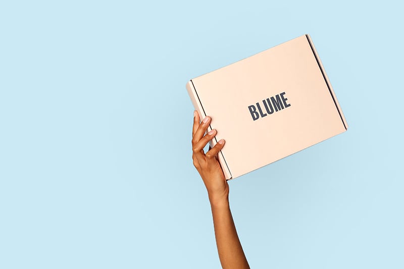 Blume box held up by a hand on a blue background