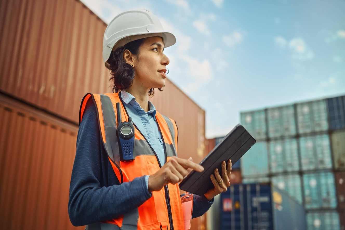 Woman in safety gear standing amongst freight containers