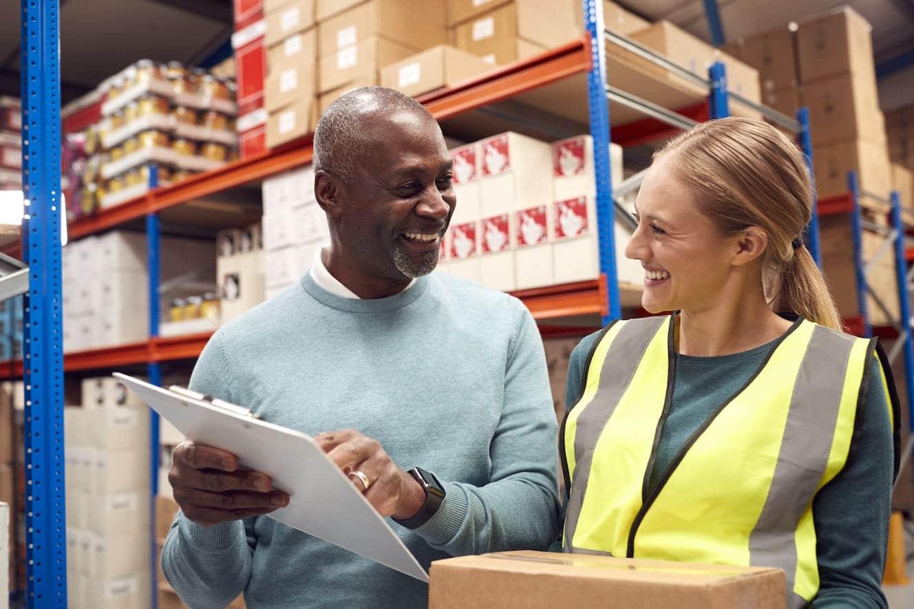 People in warehouse looking at clipboard smiling